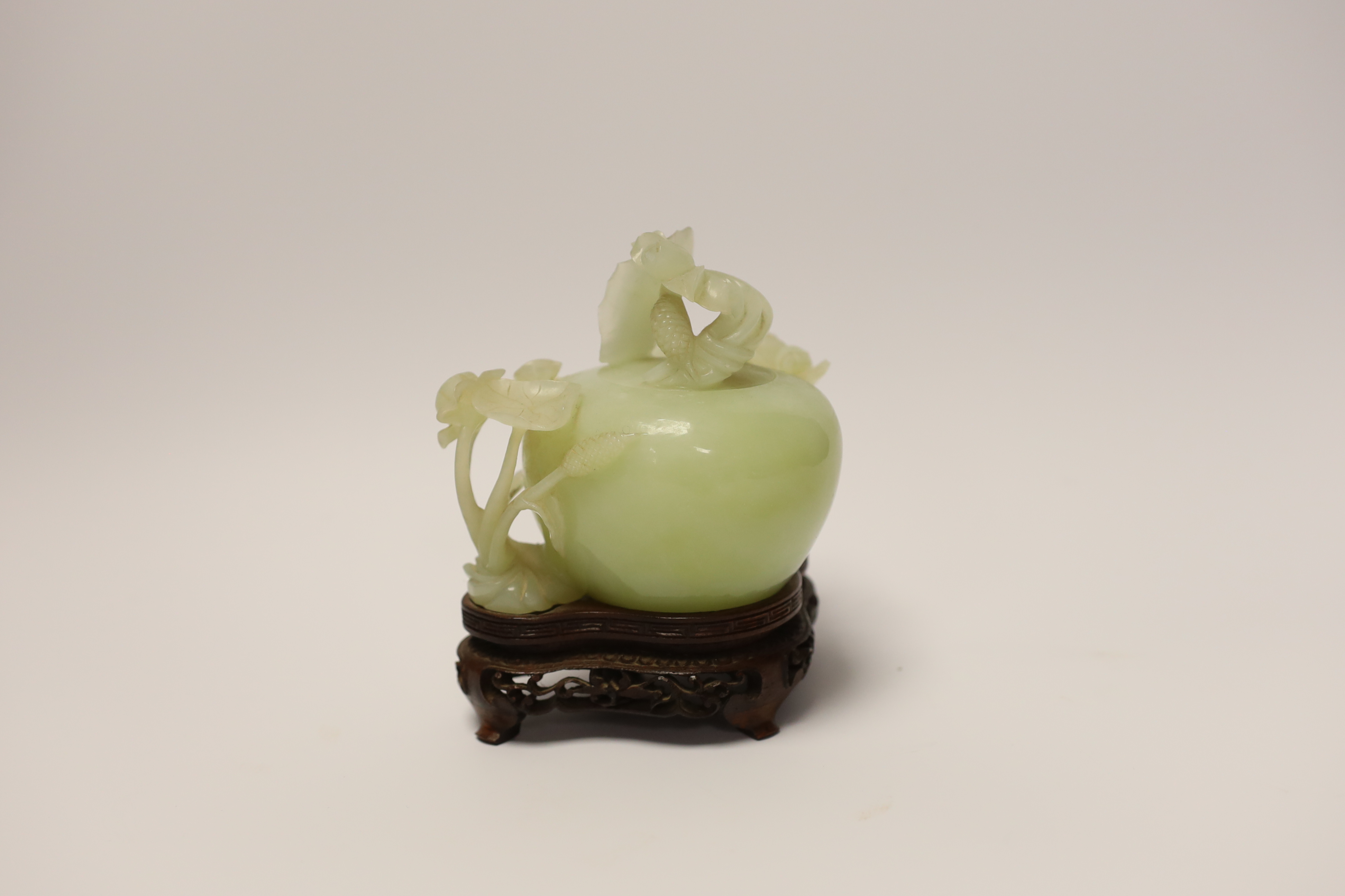 A Chinese carved bowenite jade ‘lotus’ water pot and cover on hardwood stand, 13cm